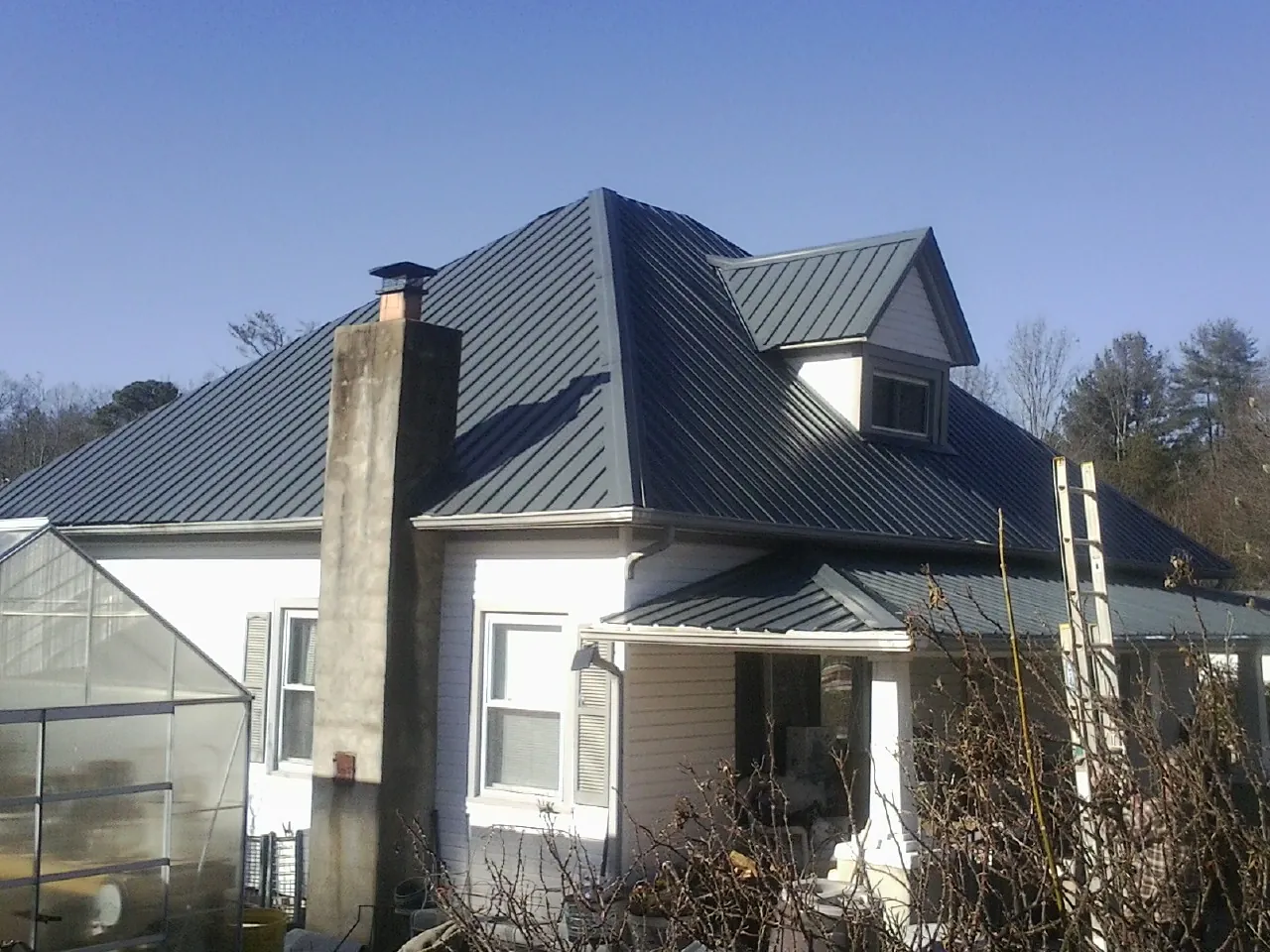 Dark blue standing seam metal roof on a white farmhouse with dormer — Slate & Tile Roof Repair by Roofing Brothers in Saxapahaw