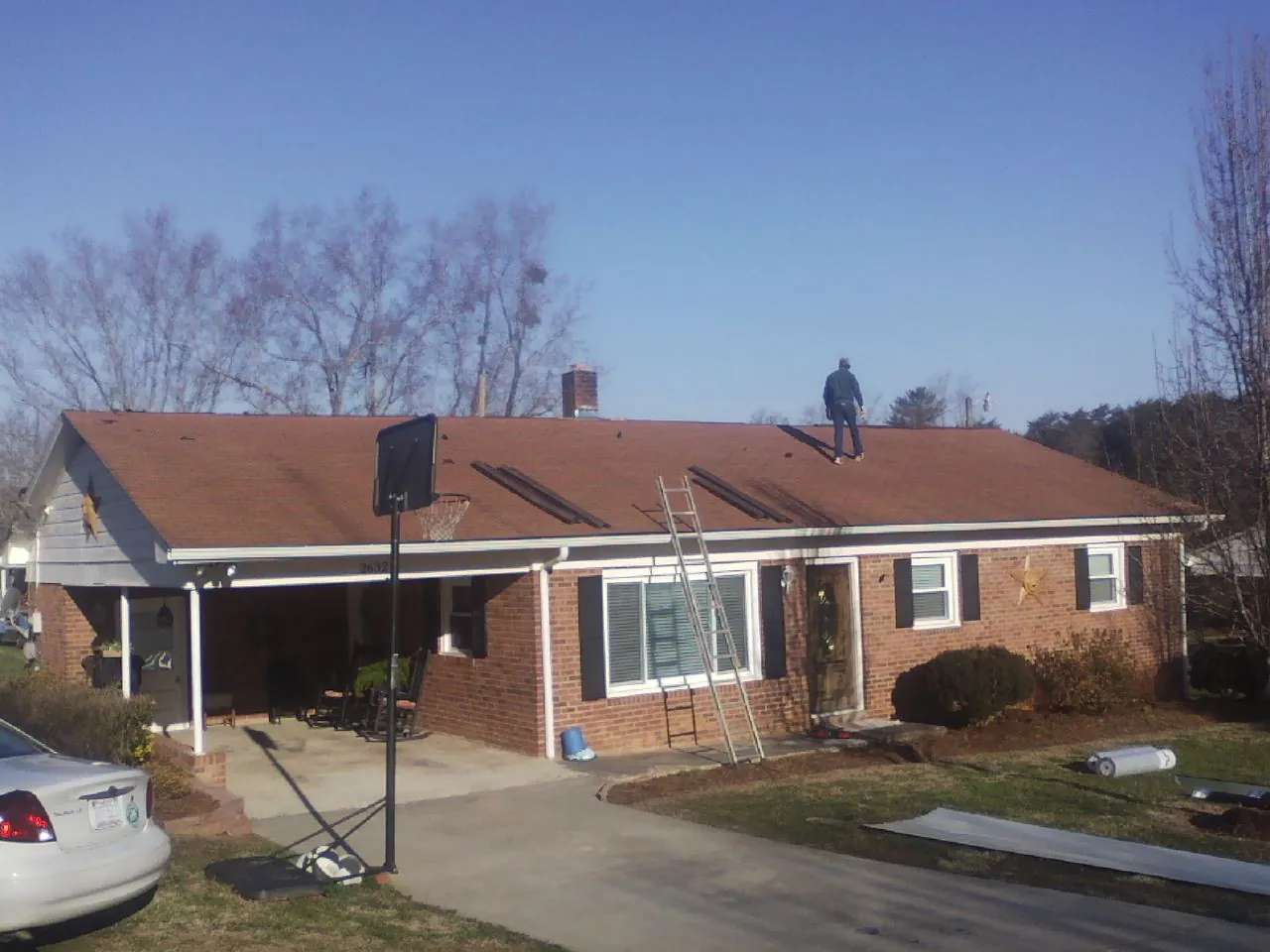 Roofer stripping a shingle roof on a brick ranch before metal panels in Saxapahaw
