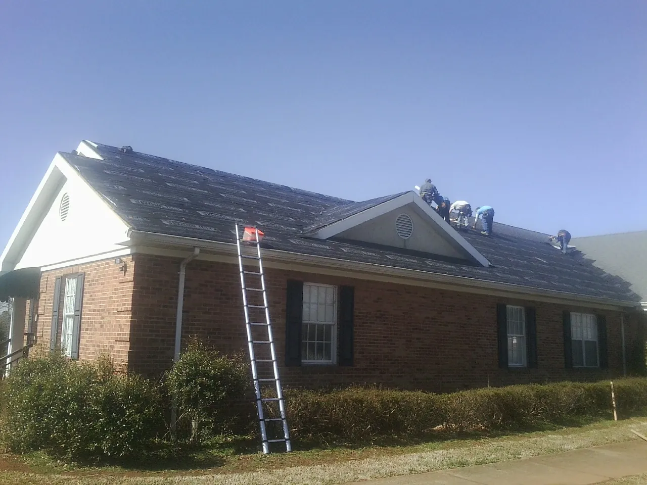 Crew tearing shingles off a brick ranch roof with a ladder set — Emergency Roof Repair work by our crew in Saxapahaw