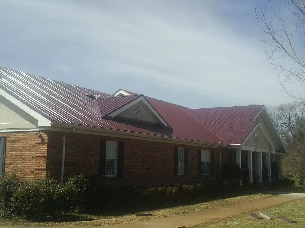 Red metal roof with gabled entries on a long brick building, from a Hail Damage Roof Repair job in Saxapahaw