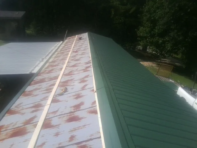 Old rusted panels beside newly installed green metal roofing — Wind Damage Roof Repair by Roofing Brothers in Saxapahaw