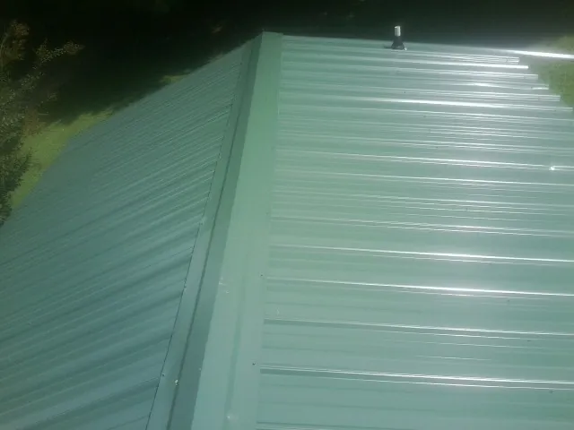 New green metal panels meeting at the ridge of a roof — Flat Roof Repair work by our crew in Saxapahaw