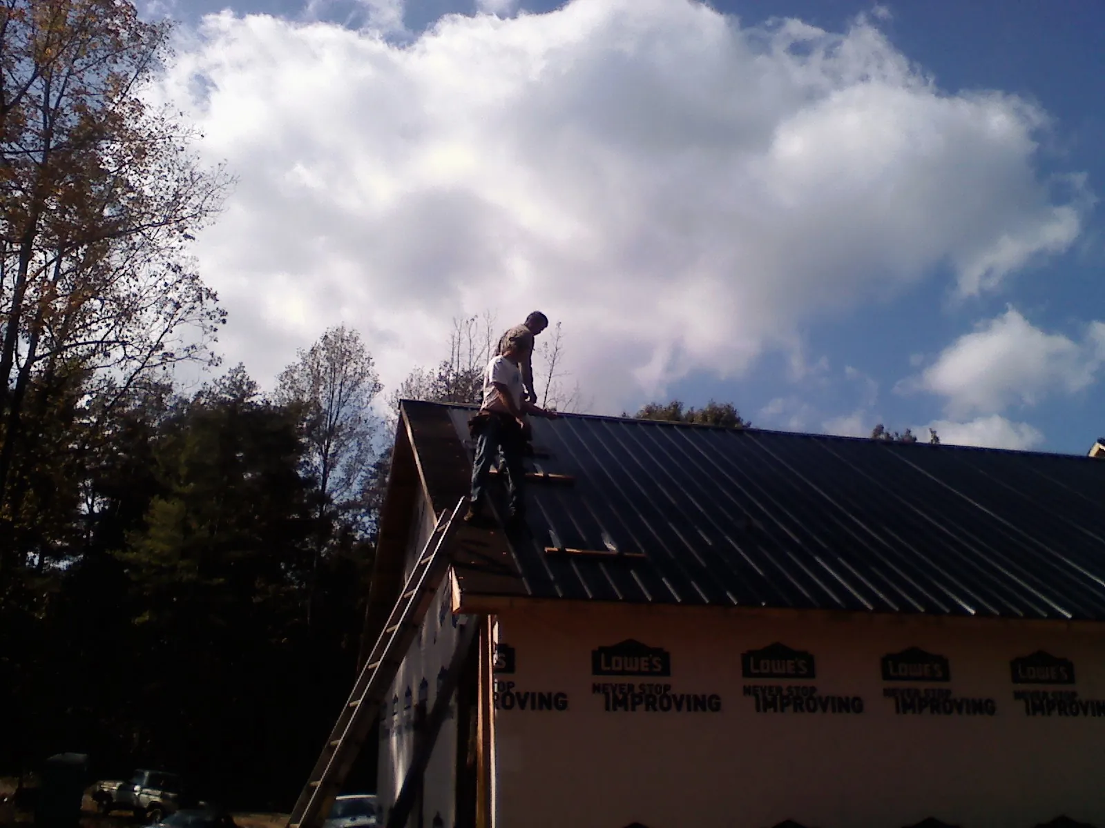 Roofer fastening dark metal panels high against a cloudy sky, from a Roof Inspection job in Saxapahaw