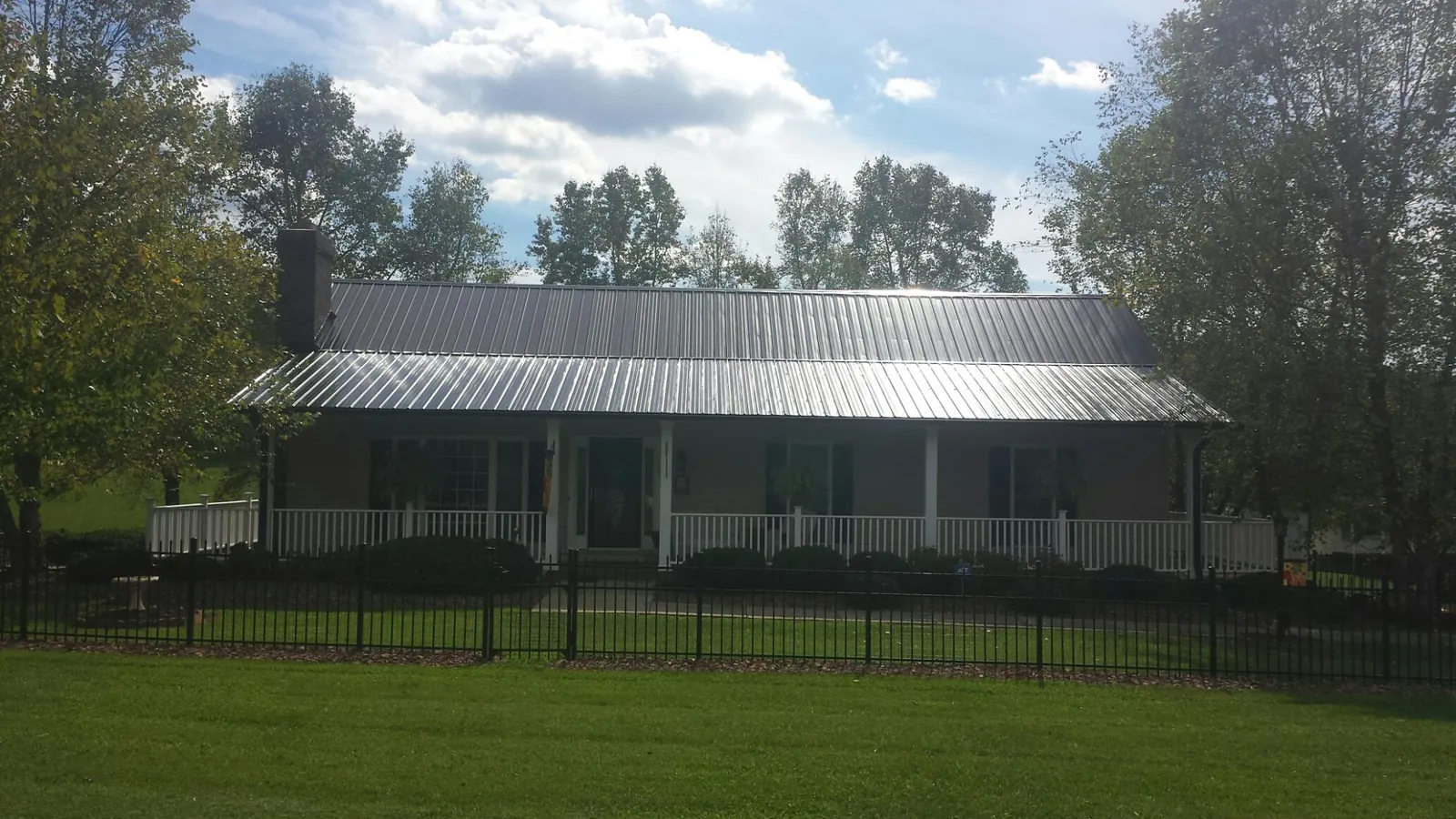Gray metal roof on a brick ranch with a full width front porch — Gutter Guard Installation work by our crew in Saxapahaw