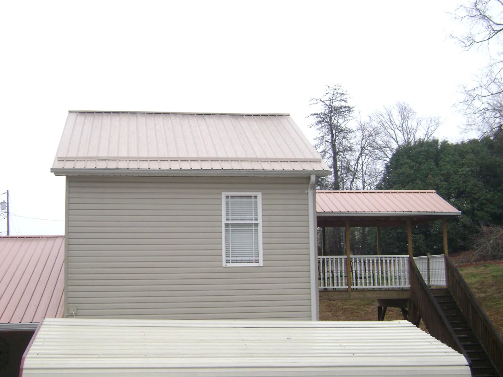 Tan metal roofs on a two story addition and attached porch, from a Roof Replacement job in Saxapahaw